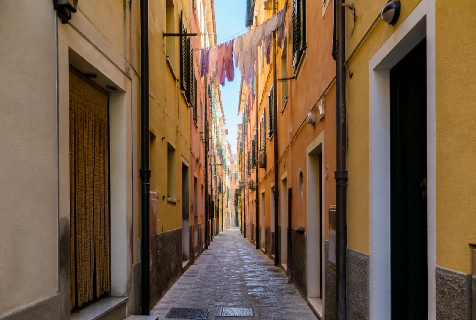 Caruggio stretto di un centro storico, case pastello, panni stesi in alto e una striscia di cielo
