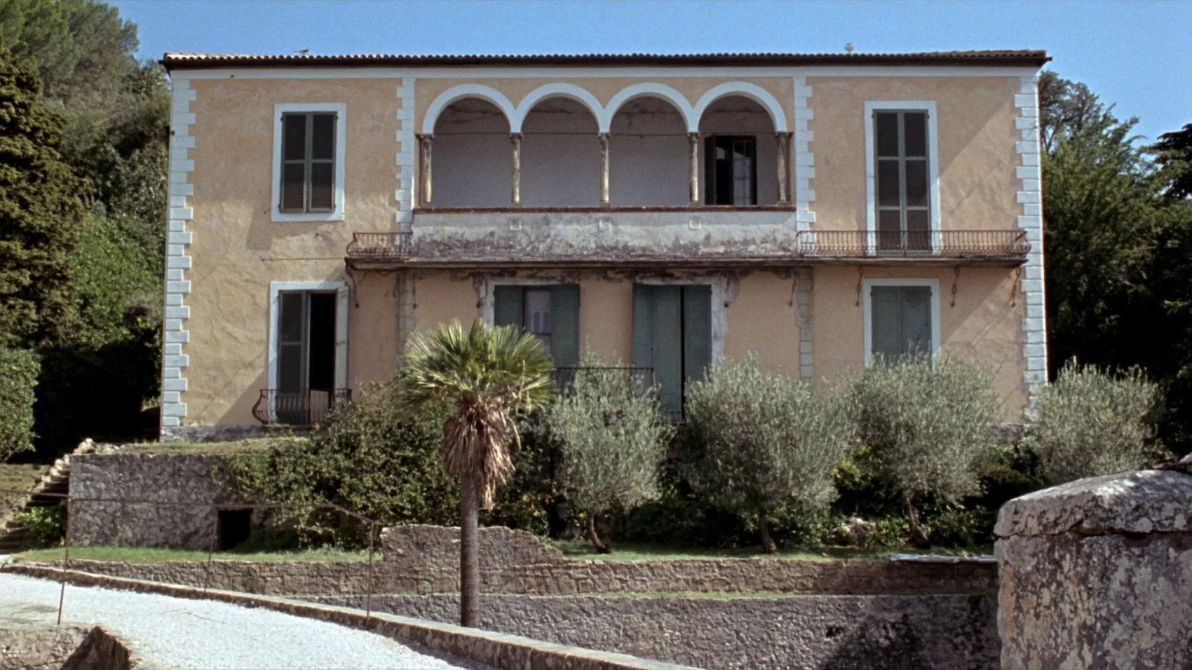 Facciata simmetrica di una villa ottocentesca color ocra, con loggia a quattro archi al piano nobile, intonaco scrostato e giardino a terrazze davanti