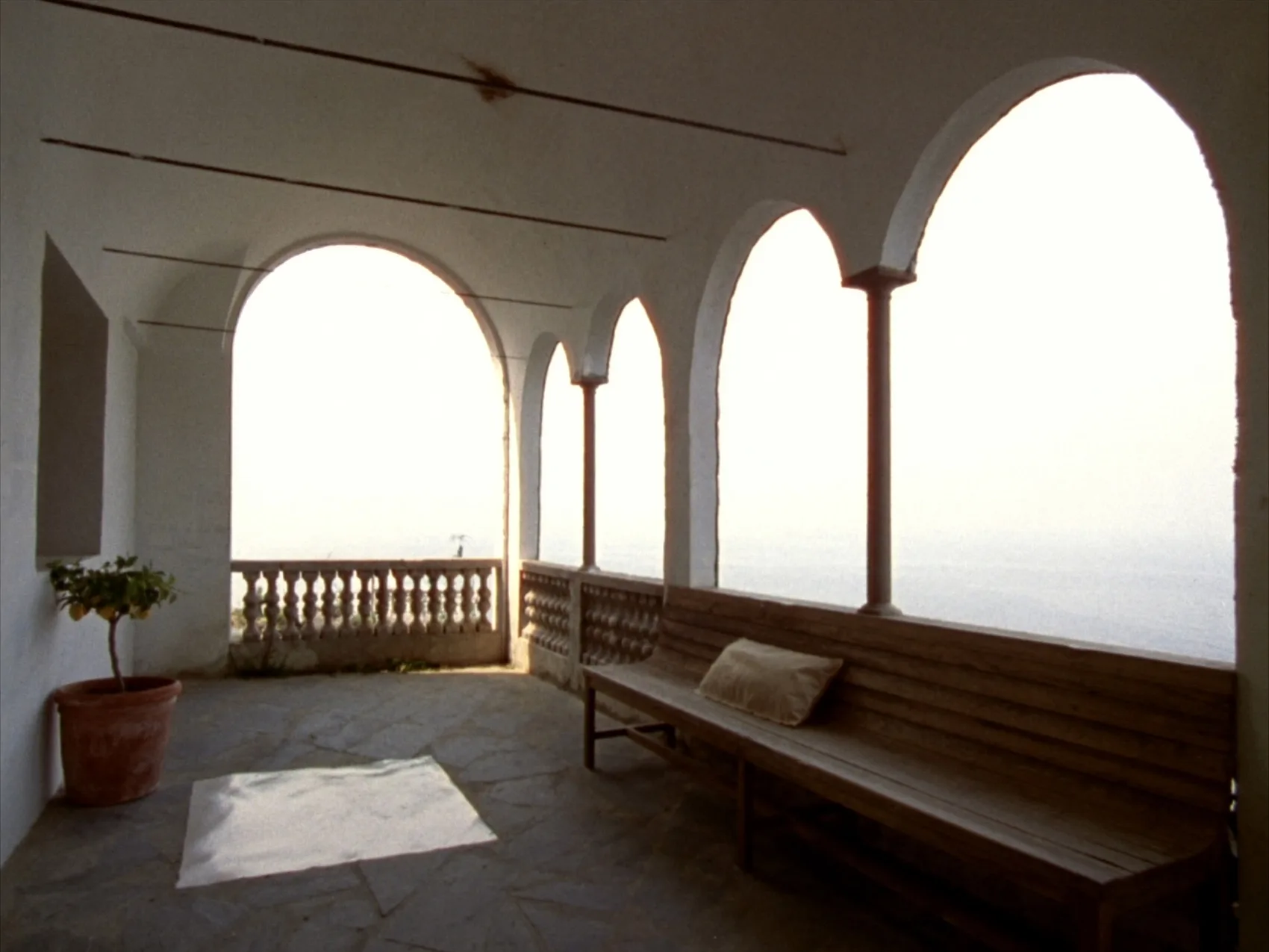 Loggia con quattro archi su colonne, panca di legno lungo il parapetto, un limone in vaso e il mare che riempie tutte le aperture