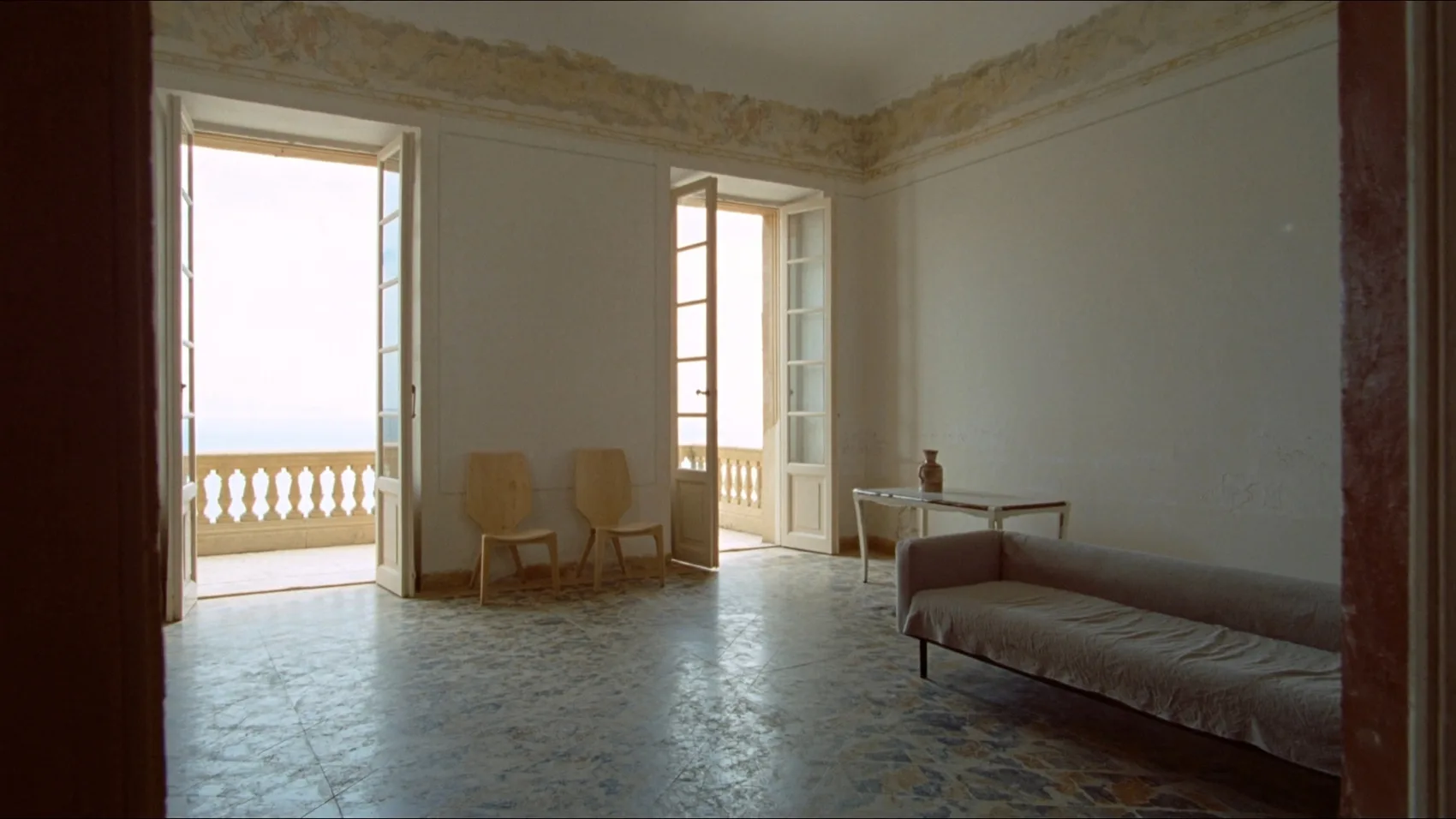 Salone vuoto con pavimento a terrazzo veneziano, due portefinestre aperte sulla balaustra e cornice affrescata sotto il soffitto